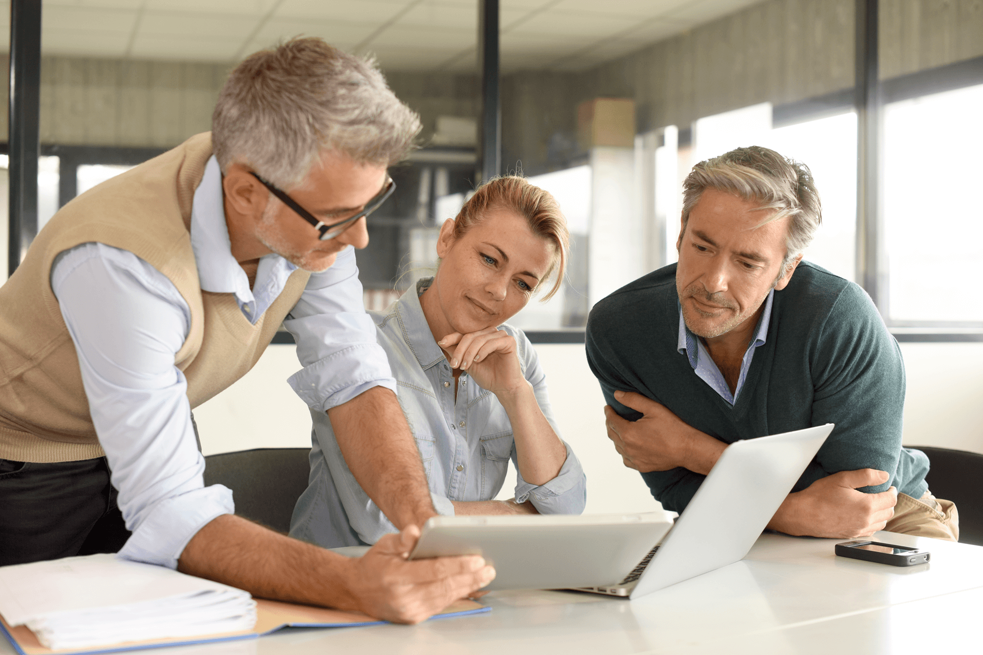 Three people looking at a laptop and tablet